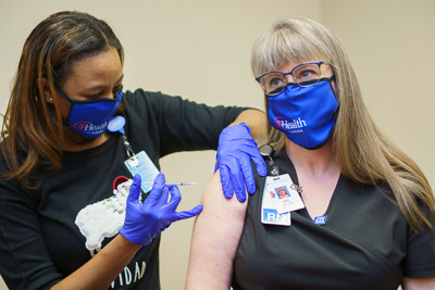 Janet Bennett, R.N., a nurse in the observation unit at UF Health The Villages® Hospital, received the hospital’s inaugural COVID-19 vaccination Dec. 17, 2020 as local media, UF Health Central Florida leaders and staff looked on. The shot was administered by hospital pharmacist Erika Jasper, Pharm.D.